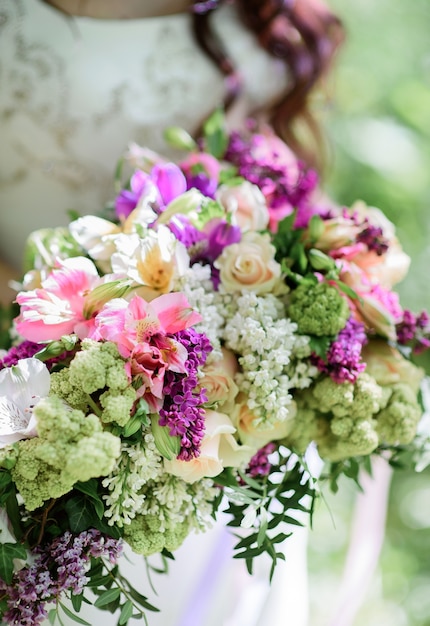Panna młoda trzyma bogaty bukiet ślubny wykonany z białych i fioletowych kwiatów