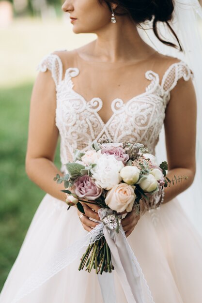 Panna młoda trzyma piękny bukiet ślubny z różami i piwoniami