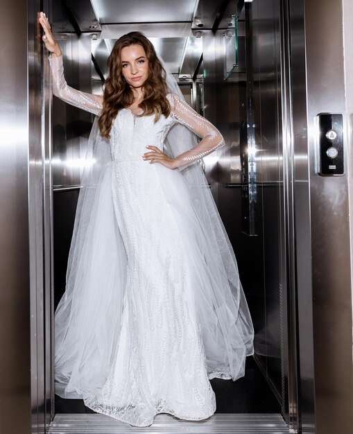 Panna młoda w sukni pozuje na tle metalowych drzwi windy