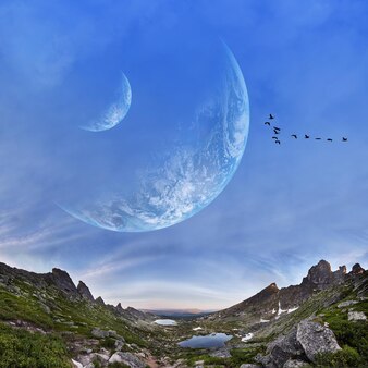 Panoramiczne góry i dwie planety na niebie. fantastyczny świat, ptaki latające na tle planet lub księżyców. zachód słońca odbija się w chmurach