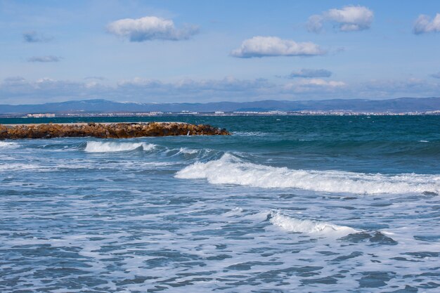 Panoramiczne ujęcie oceanu z falami tocznymi i kamiennym dokiem pod zachmurzonym niebem