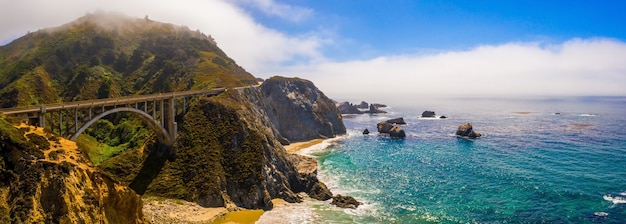 Panoramiczne ujęcie z lotu ptaka mostu California Bixby na zielonym wzgórzu w pobliżu pięknej błękitnej wody