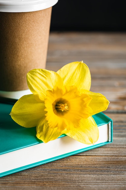 Bezpłatne zdjęcie papierowa filiżanka książka i żółty kwiat na zamazanym drewnianym tle