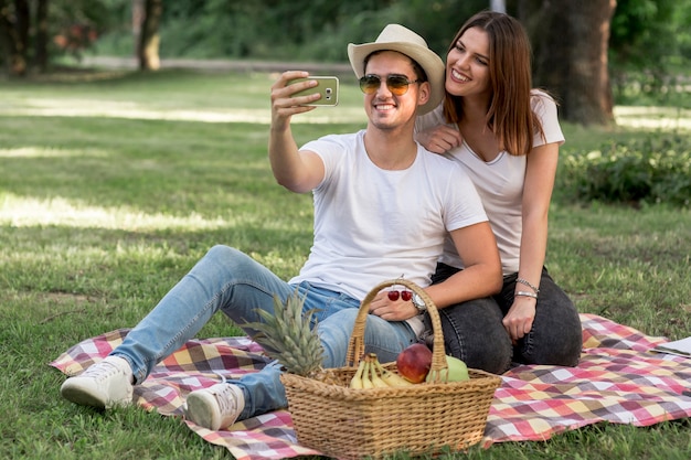 Bezpłatne zdjęcie para biorąc selfie i uśmiechając się na piknik