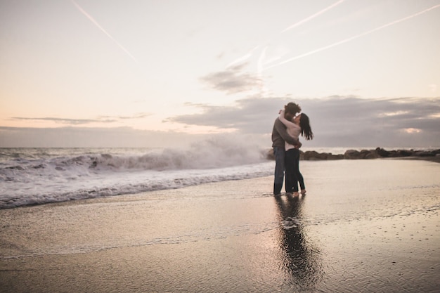 Bezpłatne zdjęcie para całuje na brzegu plaży o zachodzie słońca