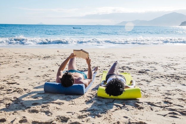 Bezpłatne zdjęcie para leżącego i czytania na plaży