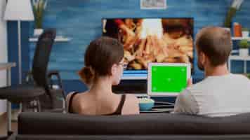 Bezpłatne zdjęcie para relaks na kanapie, patrząc na treści wideo w mediach społecznościowych za pomocą cyfrowego tabletu z zielonym ekranem w salonie. mężczyzna i kobieta cieszą się wolnym czasem oglądając vloga z influencerami na urządzeniu z kluczem chrominancyjnym.