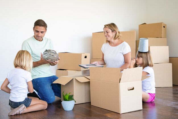 Para rodzinna i małe dziewczynki przeprowadzają się do nowego mieszkania, bawią się przy rozpakowywaniu rzeczy w nowym mieszkaniu, siedząc na podłodze i wyjmując przedmioty z otwartych pudeł