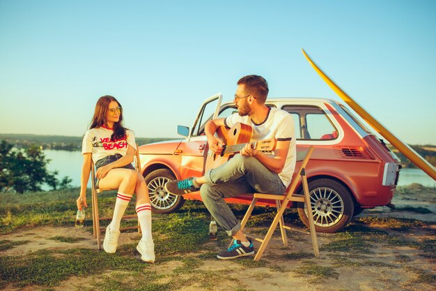 Para siedzi i odpoczywa na plaży, grając na gitarze w letni dzień, w pobliżu rzeki