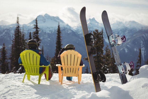 Para siedzi na krześle przez deski snowboardowe w górach pokryte śniegiem