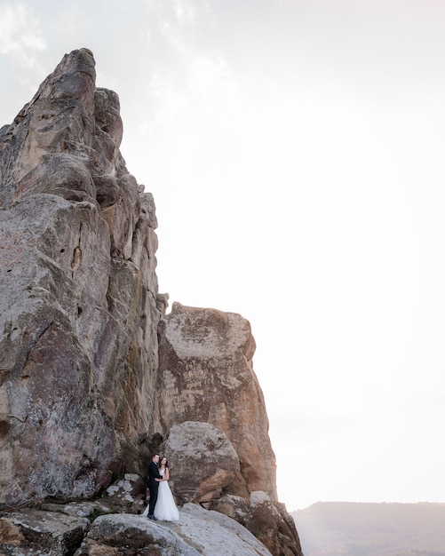 Para ślub stoi w pobliżu wysokiego klifu i przytulanie, wycieczka ślubna, zdjęcie ślubne