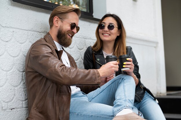 Para w kurtkach ze skóry syntetycznej pijąca razem kawę na świeżym powietrzu