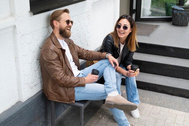 Para w kurtkach ze skóry syntetycznej pijąca razem kawę na świeżym powietrzu