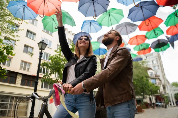 Bezpłatne zdjęcie para w kurtkach ze skóry syntetycznej przechodząca pod kolorowymi parasolami na zewnątrz