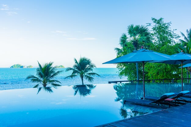 Parasol i krzesło wokoło pięknego luksusowego plenerowego pływackiego basenu z dennym widok na ocean w hotelowym kurorcie dla wakacje wakacje podróży