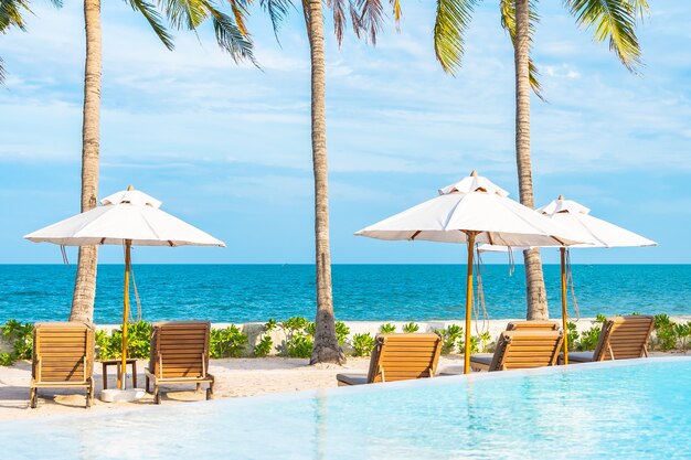 Parasol i leżak wokół odkrytego basenu w hotelowym kurorcie z plażą morską i palmą kokosową