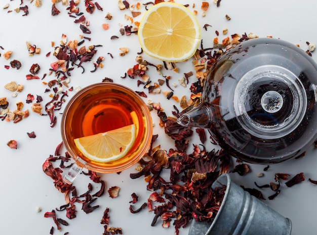 Parzona herbata z suszonymi ziołami, cytryną w szkle i czajnikiem na białej powierzchni