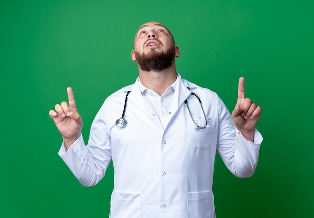 Bezpłatne zdjęcie patrząc na młodego lekarza mężczyznę noszącego szatę medyczną i wskazujący na stetoskoposcope