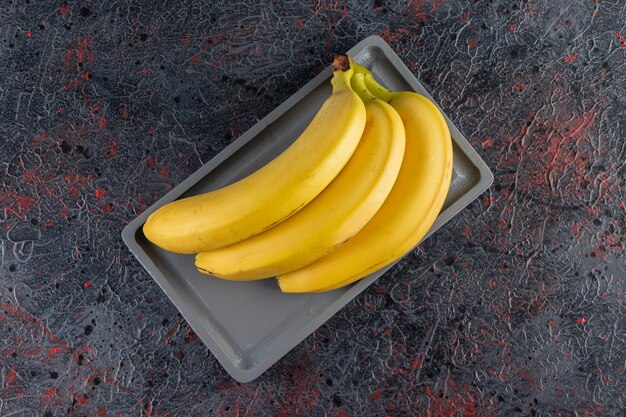 Pęczek soczystego żółtego banana ułożony na ciemnym talerzu.