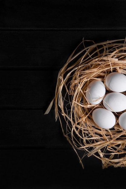 Pęczek surowych świeżych jaj w ptasie gniazdo na czarnej powierzchni. Wysokiej jakości zdjęcie