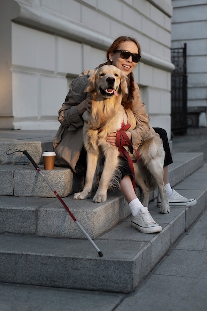 Pełen strzał uśmiechniętej kobiety pieszczącej psa usługowego