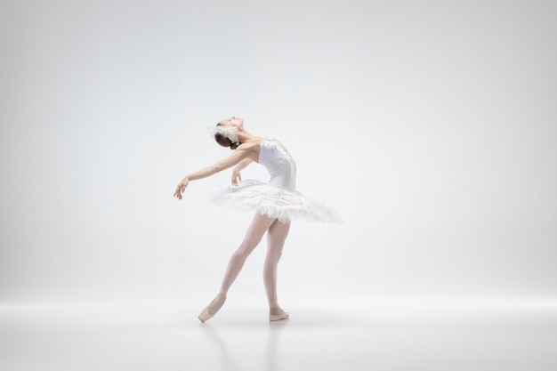 Pełen wdzięku klasyczny taniec baleriny na białym tle na tle białego studia. kobieta w delikatnych ubraniach przypominających białe łabędzie. koncepcja łaski, artysty, ruchu, akcji i ruchu. wygląda nieważko.