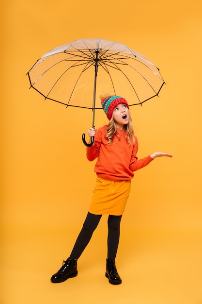 Pełna długość Młoda dziewczyna w swetrze i kapeluszu z parasolem czeka deszcz nad pomarańczą