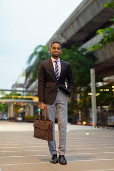 Pełna długość portret przystojnego młodego afrykańskiego biznesmena na zewnątrz w mieście