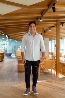 Pełna Długość Portret Przystojny Perski Mężczyzna Uśmiechający Się I Stojący W Kawiarni Premium Zdjęcia