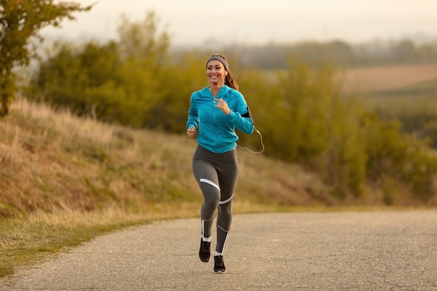Bezpłatne zdjęcie pełna długość szczęśliwej sportsmenki biegającej rano na drodze skopiuj miejsce