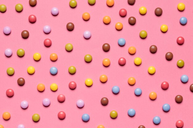 Pełna rama kolorowi stubarwni klejnotów cukierki na różowym tle