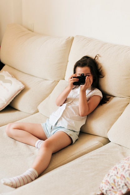 Bezpłatne zdjęcie pełna strzał dziewczyna na kanapie z aparatem fotograficznym