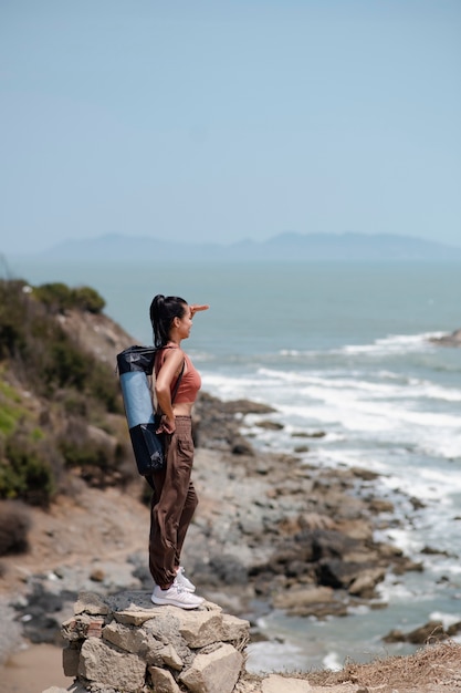 Pełna strzał kobieta z matą do jogi nad morzem