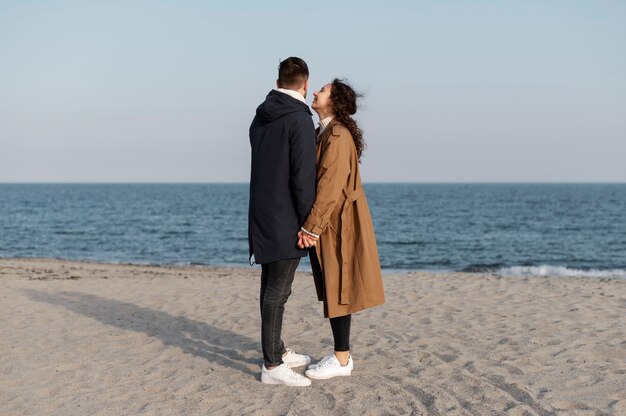 Pełna strzał para trzymająca się za ręce na plaży