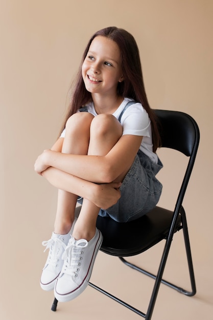 Pełna strzał uśmiechnięta dziewczyna siedzi na krześle