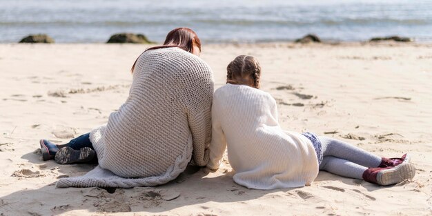 Pełne ujęcie matki i dziecka siedzącego na piasku