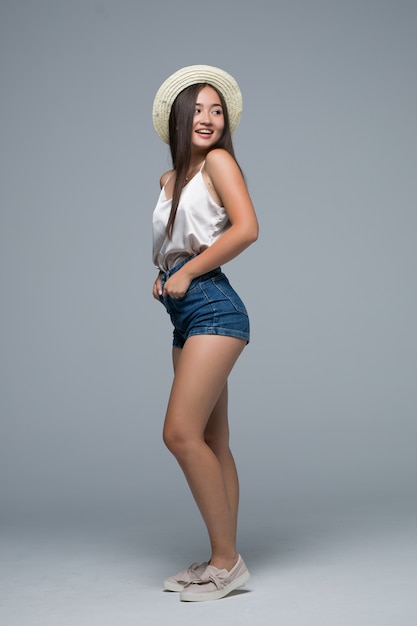 Pełnego wzrosta azjatykcia dziewczyna w słomianym kapeluszu na szarym tle