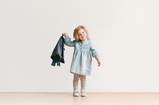 Bezpłatne zdjęcie pełnej długości portret słodkie małe dziecko dziewczynka w stylowe dżinsy ubrania i uśmiechnięty, stojący na białym tle. koncepcja mody dla dzieci