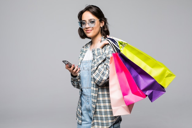 Pełnej długości portret szczęśliwa młoda kobieta trzyma torby na zakupy i telefon komórkowy na białym tle