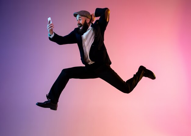Pełnej długości portret szczęśliwego skaczącego mężczyzny w neonowym świetle i gradiencie