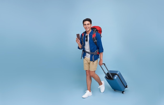 Pełnej długości Szczęśliwy uśmiechnięty młody turysta Azjatycki mężczyzna spacerujący trzymając bagaż i pokazując paszport