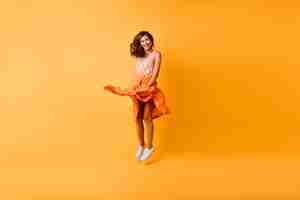 Bezpłatne zdjęcie pełnometrażowy portret stylowej kobiety debonair skaczącej w studio. wspaniała ruda dziewczyna w pomarańczowej spódnicy, zabawy.
