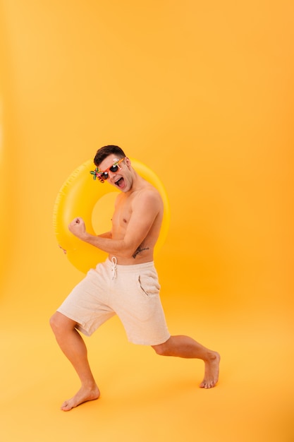 Pełny obraz radosnego nagiego mężczyzny w szortach i okularach przeciwsłonecznych