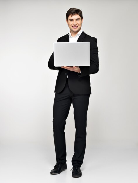 Pełny portret uśmiechnięty szczęśliwy biznesmen z laptopem w czarnym garniturze