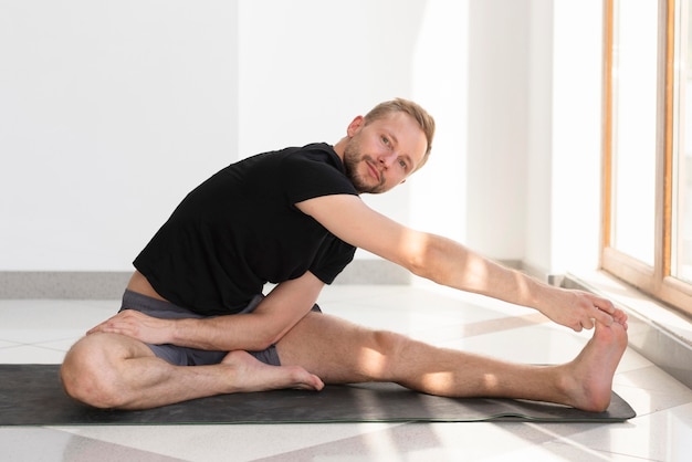 Bezpłatne zdjęcie pełny strzał człowieka rozciągającego się na macie do jogi