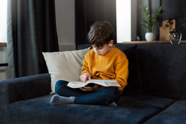 Pełny strzał małego chłopca czytającego Biblię w domu