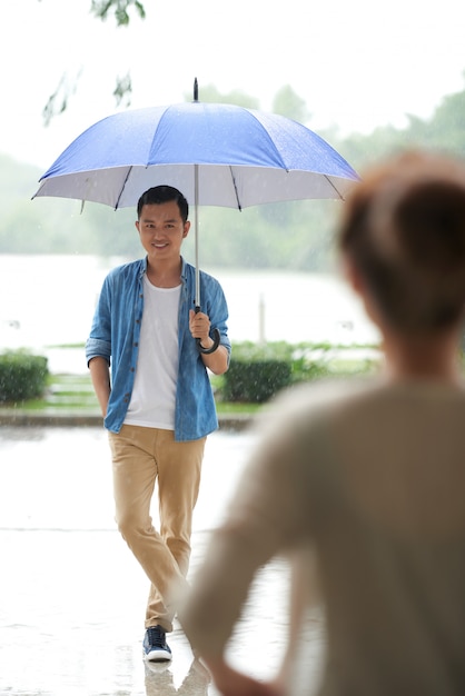 Pełny strzał mężczyzna stojący z parasolem w deszczu, czekając na swoją datę