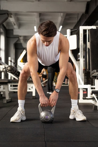 Pełny strzał mężczyzny trenujący z kettlebell na siłowni