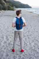 Bezpłatne zdjęcie pełny strzał nastolatka z plecakiem na plaży