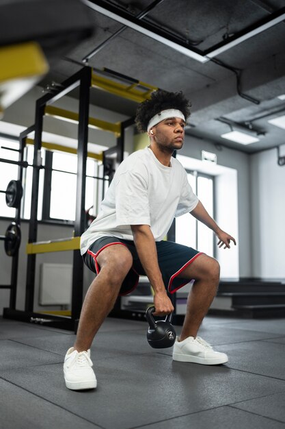 Pełny strzał sprawny mężczyzna ćwiczący z kettlebell na siłowni